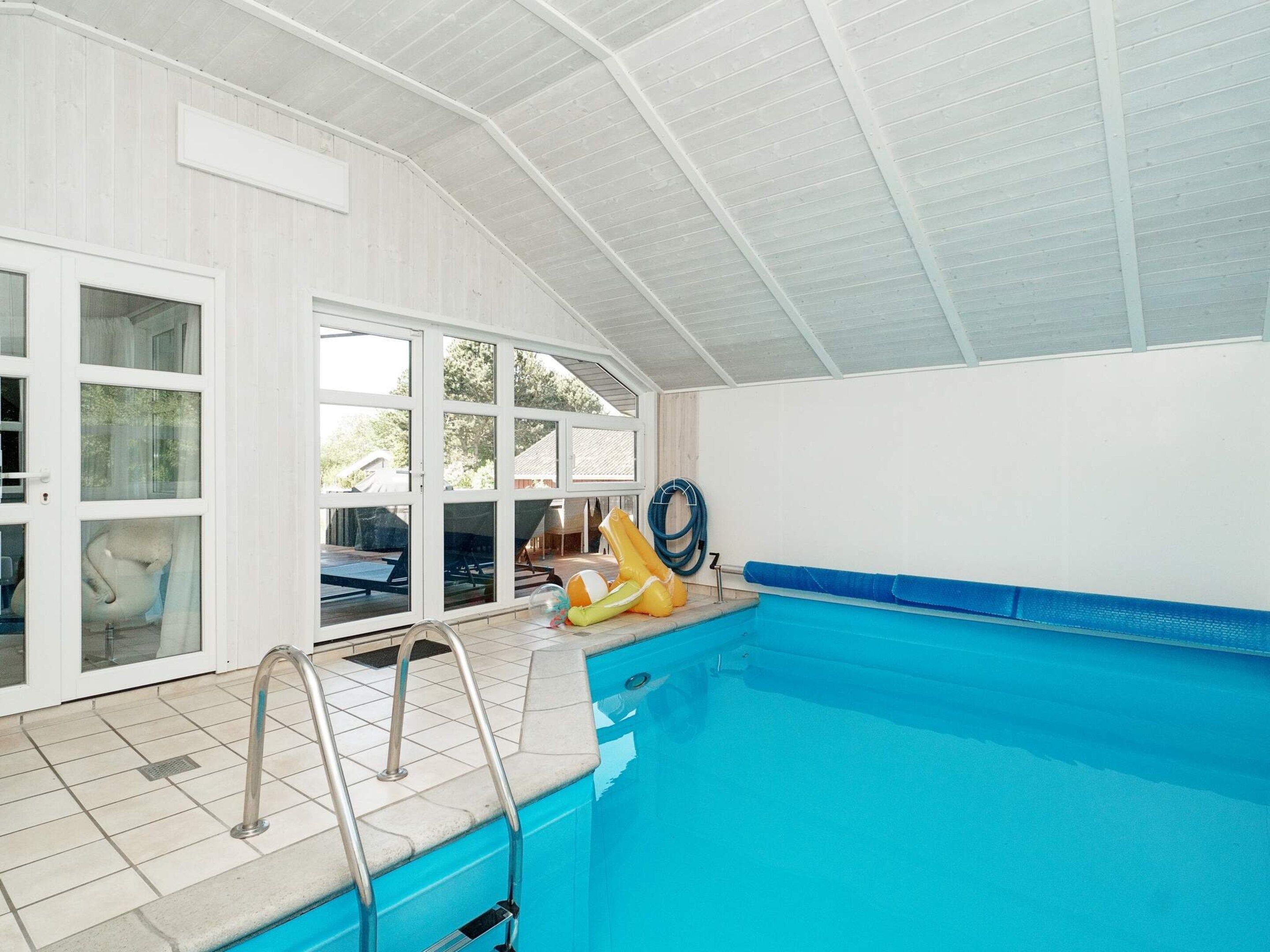 Ein überdachter Schwimmbereich mit großen Glaswänden, Fliesenboden und blauer Poolkante.