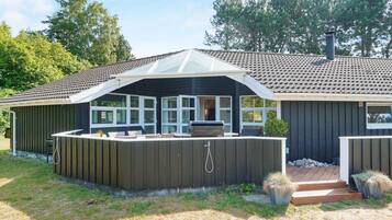 Ein Haus mit überdachter Terrasse, Grill und kleinem Garten.