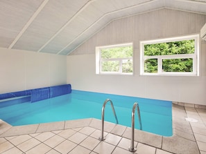 Ein Schwimmbecken mit blauer Innenauskleidung, gefliestem Boden und Metallhandläufen.
