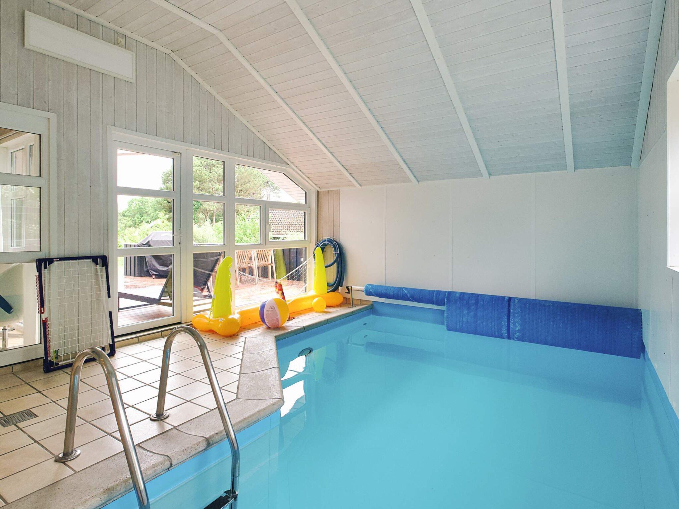 Una piscina interior con suelo de baldosas, una escalera de piscina y juguetes inflables.