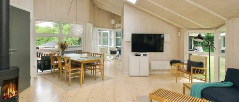 A spacious living area with a fireplace, wooden furniture, a television, and large windows.