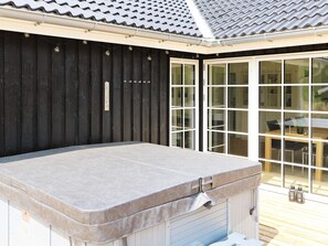 A hot tub with a wooden deck and a sliding glass door leading to a dining area. - 8 Person Holiday Home in Hadsund (Hadsund)