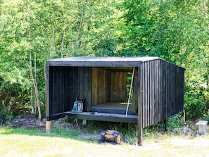 A small, wooden cabin with a slanted roof, situated in a wooded area. - 8 Person Holiday Home in Hadsund (Hadsund)