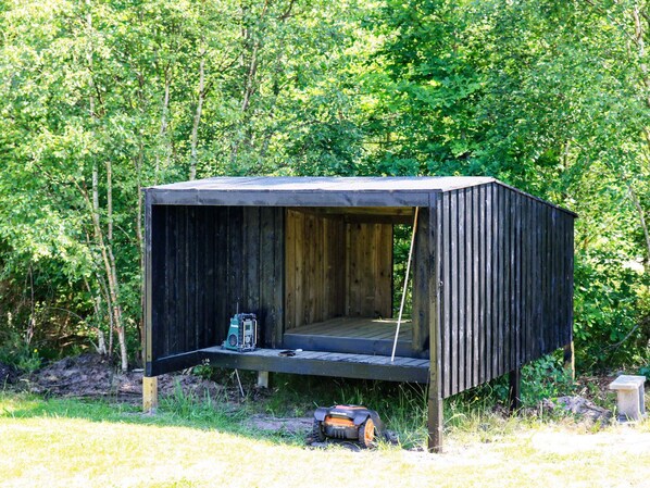 A small, wooden cabin with a slanted roof, situated in a wooded area.