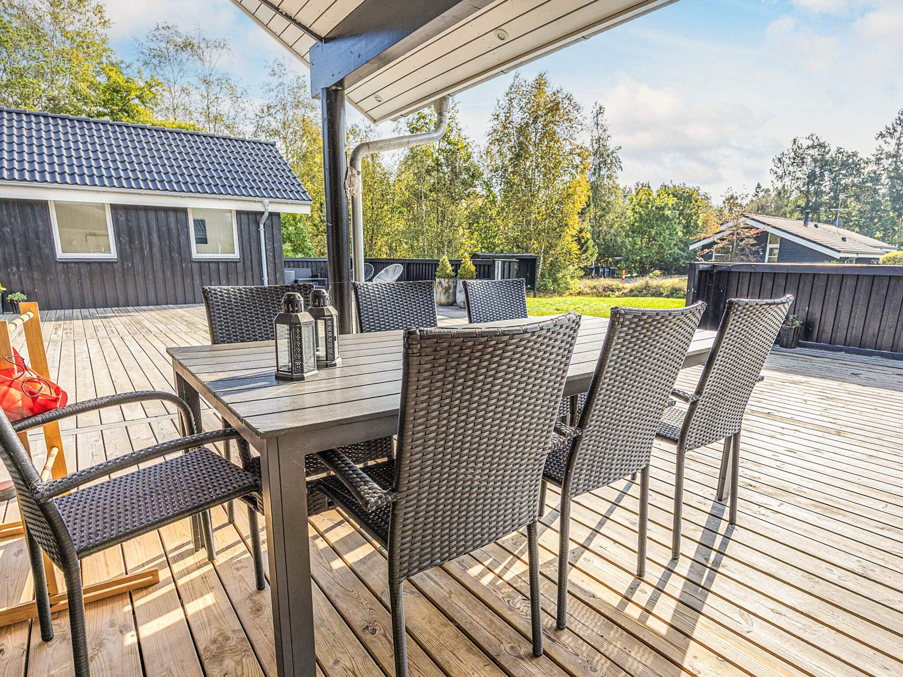 An outdoor deck with a table and chairs, surrounded by a wooden deck and a view of a house and trees.