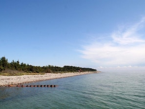 A beach with a clear sky, calm water, and a forested area in the background. - 8 Person Holiday Home in Hadsund (Hadsund)