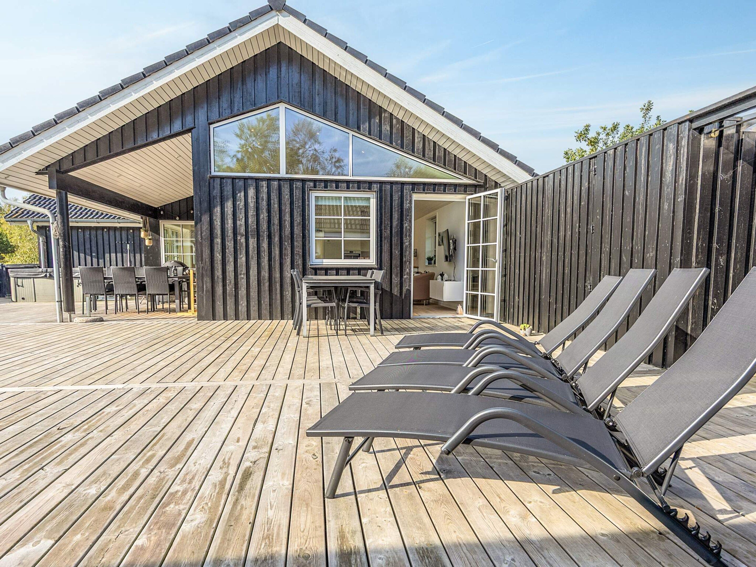 A modern wooden house with a covered patio, outdoor seating, and a pool area.