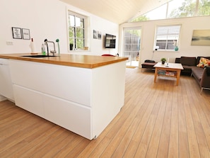 A modern kitchen with a wooden countertop and white cabinetry, a dining area with a wooden table and a sofa, and a large window providing natural light. - 8 Person Holiday Home in Hadsund (Hadsund)