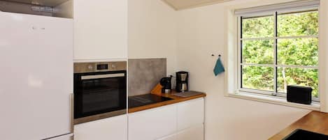 A modern kitchen with white cabinetry, a built-in oven, a coffee maker, and a window with a view of greenery.