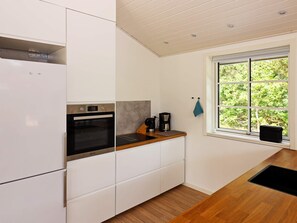 A modern kitchen with white cabinetry, a built-in oven, a coffee maker, and a window with a view of greenery.