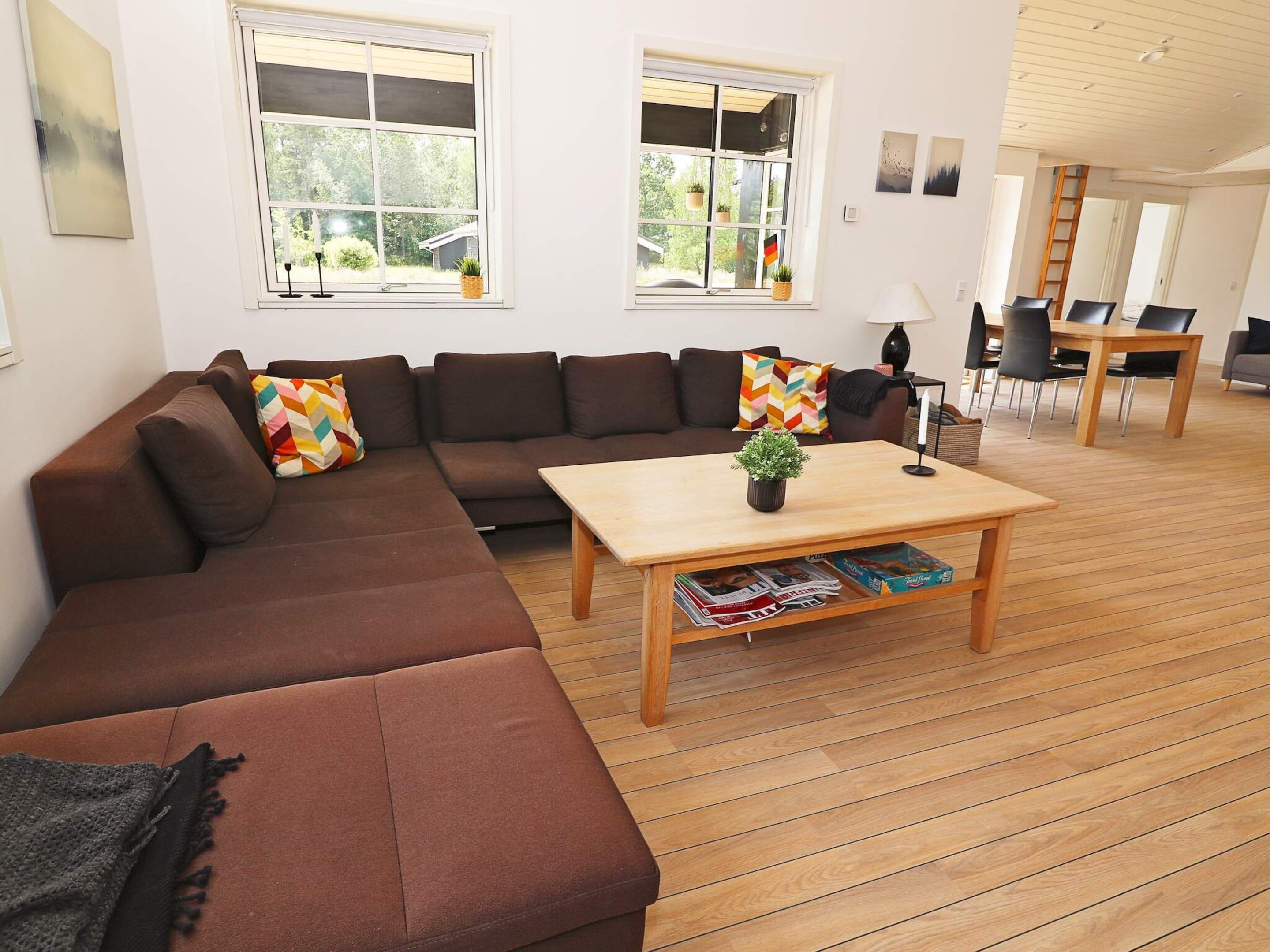 A modern living room with a sectional sofa, a coffee table with magazines, and a dining area with chairs and a table.