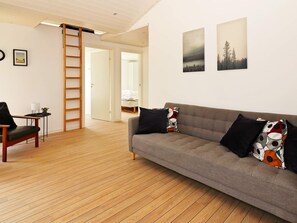 Sala de estar moderna com um sofá cinza, piso de madeira, uma escada e duas imagens emolduradas na parede.