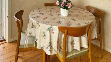 A round dining table with a floral tablecloth, surrounded by wooden chairs.