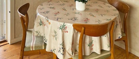 A round dining table with a floral tablecloth, surrounded by wooden chairs.