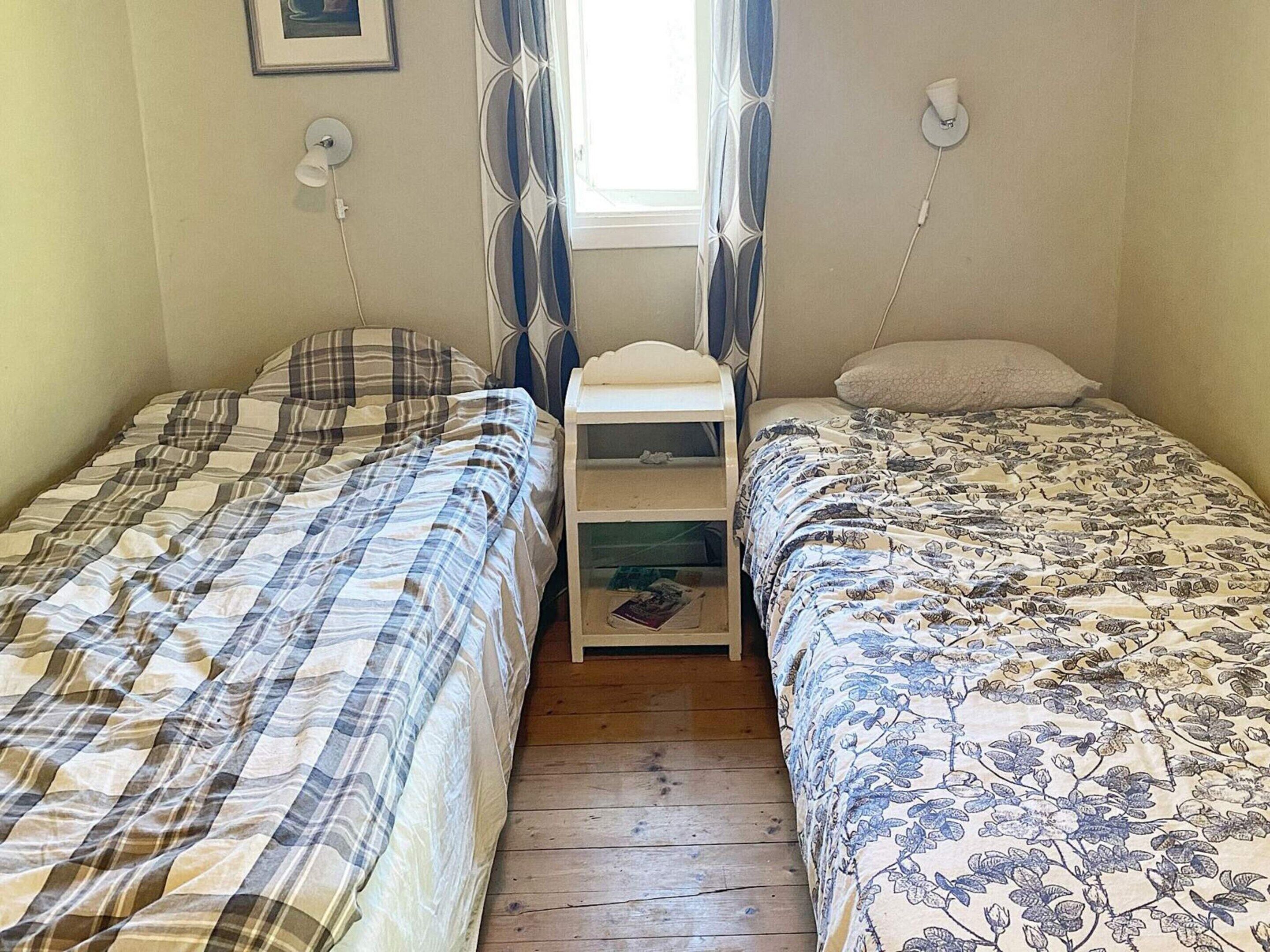 A room with two single beds, a small bedside table, and a window with curtains.