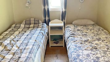 A room with two single beds, a small bedside table, and a window with curtains.