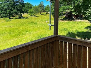 A wooden deck with a metal railing overlooking a grassy field with trees. - 4 Person Holiday Home in Vetlanda (Vetlanda)