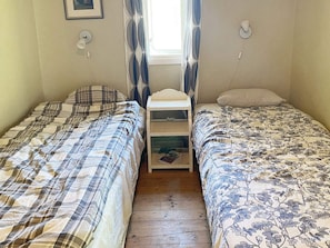 Una habitación con dos camas individuales, una mesita de noche pequeña con lámpara y una ventana con cortinas.