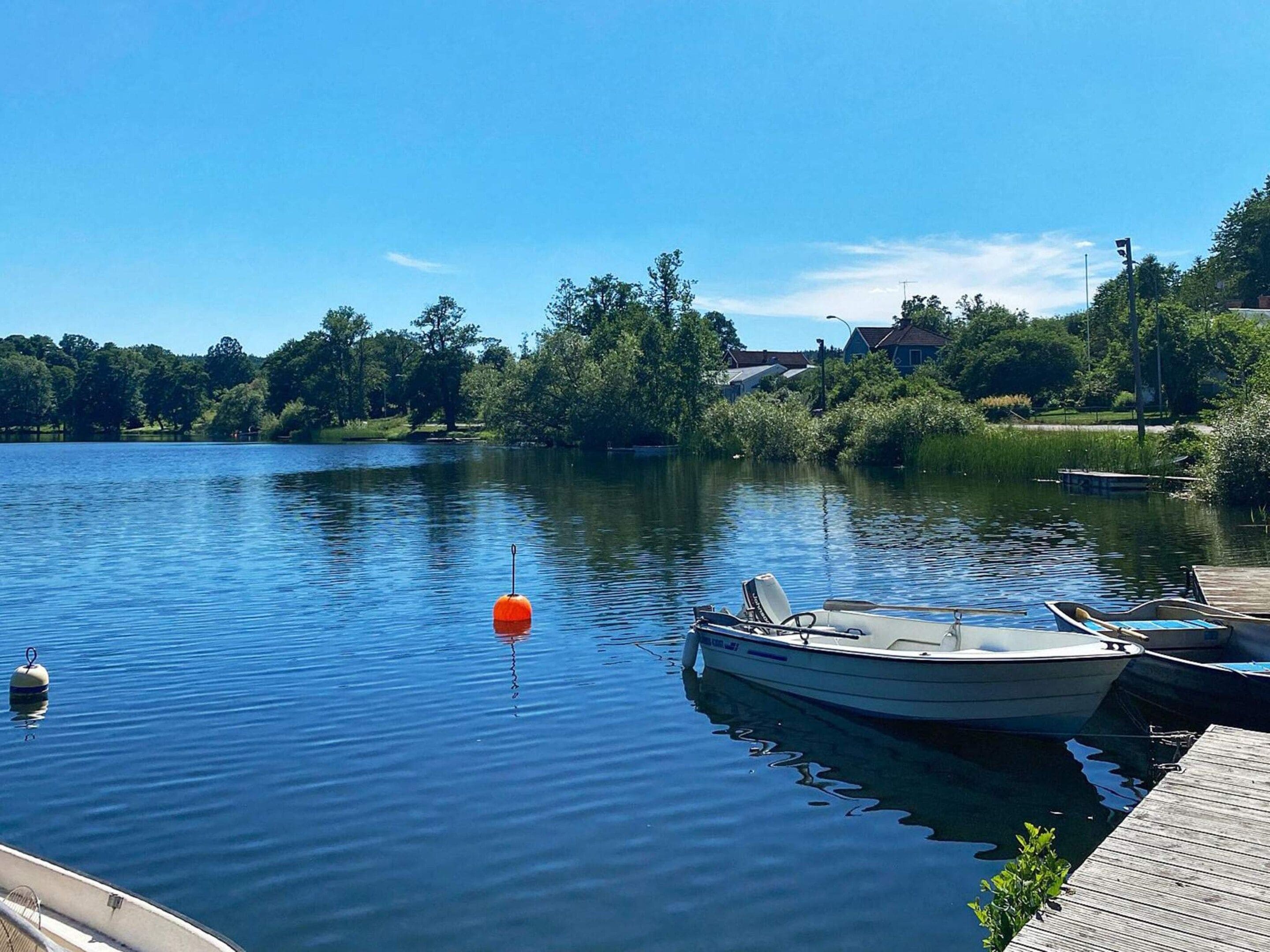 Un lago tranquilo con barcos amarrados a un muelle de madera, rodeado de árboles y un cielo despejado.