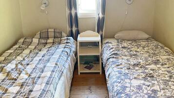 Una habitación con dos camas individuales, una mesita de noche pequeña y un ventanal con cortinas.