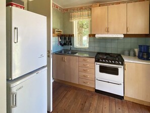 Eine Küche mit Holzausstattung, einem Kühlschrank, einem Herd und einem Fenster mit Vorhängen.