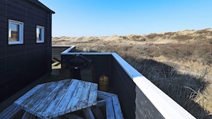 A wooden deck with a table and chairs, overlooking a dune landscape. - 2 Person Holiday Home in Brovst (Brovst)