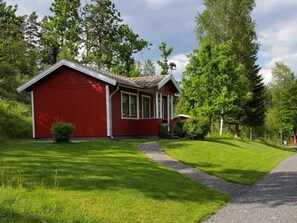 Una casa d'un pis de color vermell amb teulada inclinada, un porxo i un jardí ben cuidat.