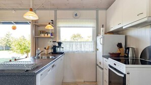 A compact kitchen with a built-in dishwasher, a stove, and a refrigerator. There are pendant lights, a window with a view, and a small countertop with a coffee maker. - 6 Person Holiday Home in Karrebaeksminde-by Traum (Karrebæksminde)