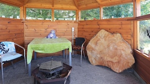 A wooden cabin with a high ceiling, a table with a green tablecloth, a chair, a large rock, and a grill. - 6 Person Holiday Home in Karrebaeksminde-by Traum (Karrebæksminde)