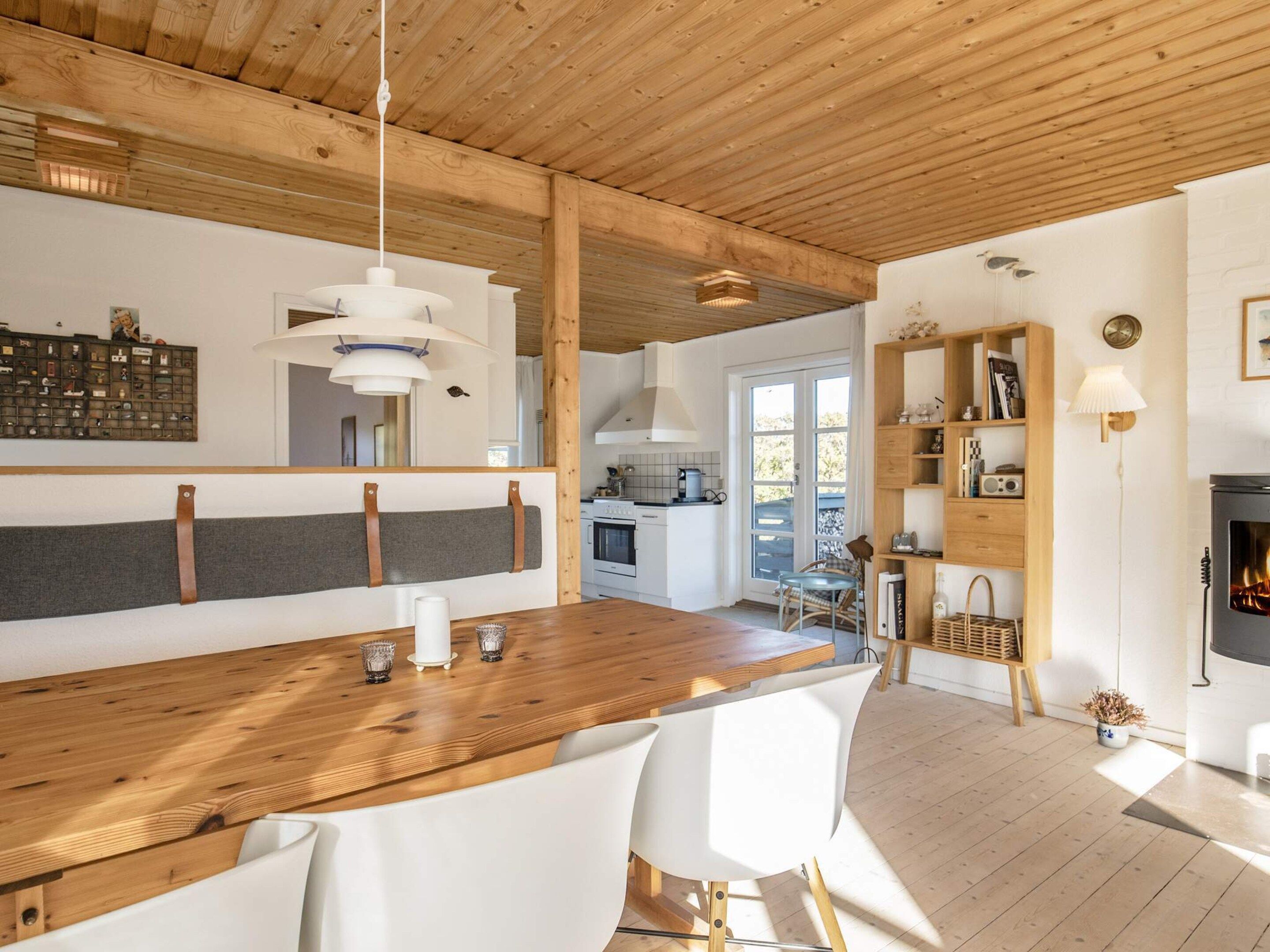 Une cuisine moderne avec un îlot central en bois, des chaises blanches, des luminaires suspendus et une cheminée.