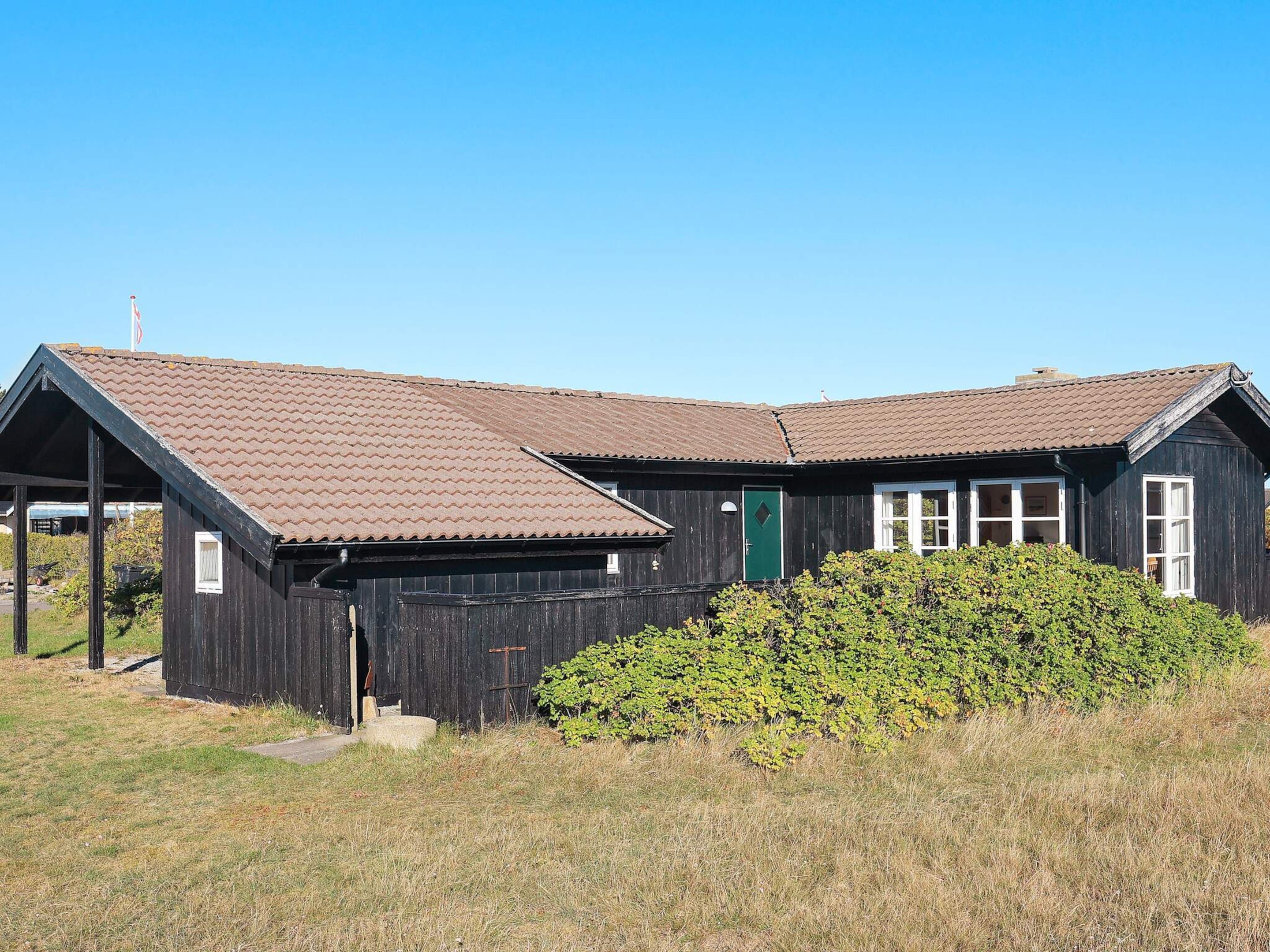 A rustic wooden building with a brown tiled roof, a green door, and a small porch area.