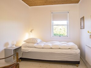 A bedroom with a bed, a nightstand, a lamp, a window, and a picture on the wall. - 4 Person Holiday Home in Skagen (Skagen)