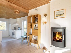 A modern kitchen with white cabinets, a stove, and a dining area with a wicker chair. - 4 Person Holiday Home in Skagen (Skagen)
