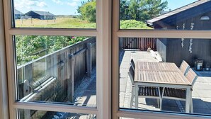 Vista a través de una ventana con una terraza de madera, una mesa y una valla.