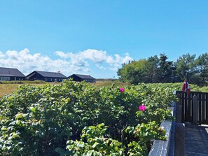 A residential area with houses, a clear sky, and a garden with green foliage and a pink flower. - 4 Person Holiday Home in Skagen (Skagen)