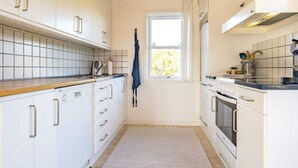 Una cocina con gabinetes blancos, techo de madera, una ventana con cortinas y salpicadero de azulejos.