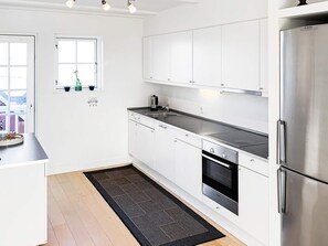Une cuisine moderne avec des meubles blancs, des appareils en acier inoxydable et un tapis aux motifs noirs et gris.