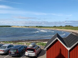 Ein Küstenparkplatz mit Autos und einem roten Gebäude mit Blick auf das Meer.