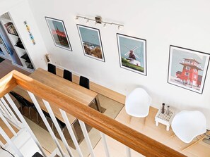 Un coin repas avec une table en bois, des chaises blanches et des tableaux représentant des moulins à vent accrochés au mur.