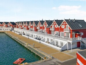 A row of red and white buildings with balconies, a pier extending into the water, and a small boat docked at the end. - 5 Star Holiday Home in Bagenkop (Sydlangeland)