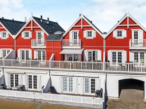 Une rangée de bâtiments rouges, ornés de bordures blanches et dotés de balcons, reliés par un pont blanc muni de garde-corps.