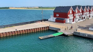 Un hôtel situé au bord de l’eau, doté d’une jetée qui s’avance sur l’eau, d’un bâtiment rouge aux ornements blancs et offrant une vue dégagée sur la mer.