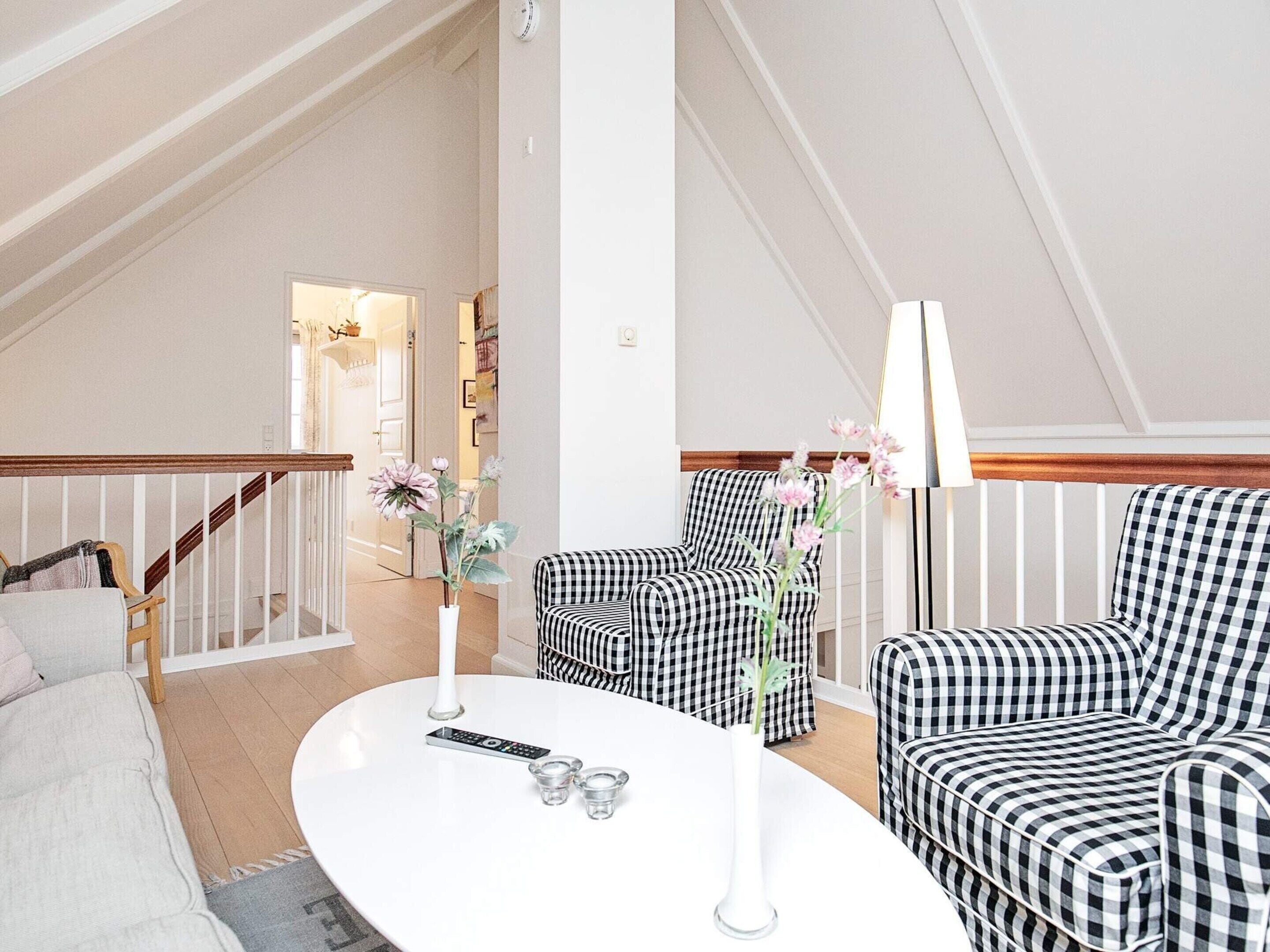 A living room with a white round coffee table, two checkered armchairs, a sofa, and a staircase leading to another room.