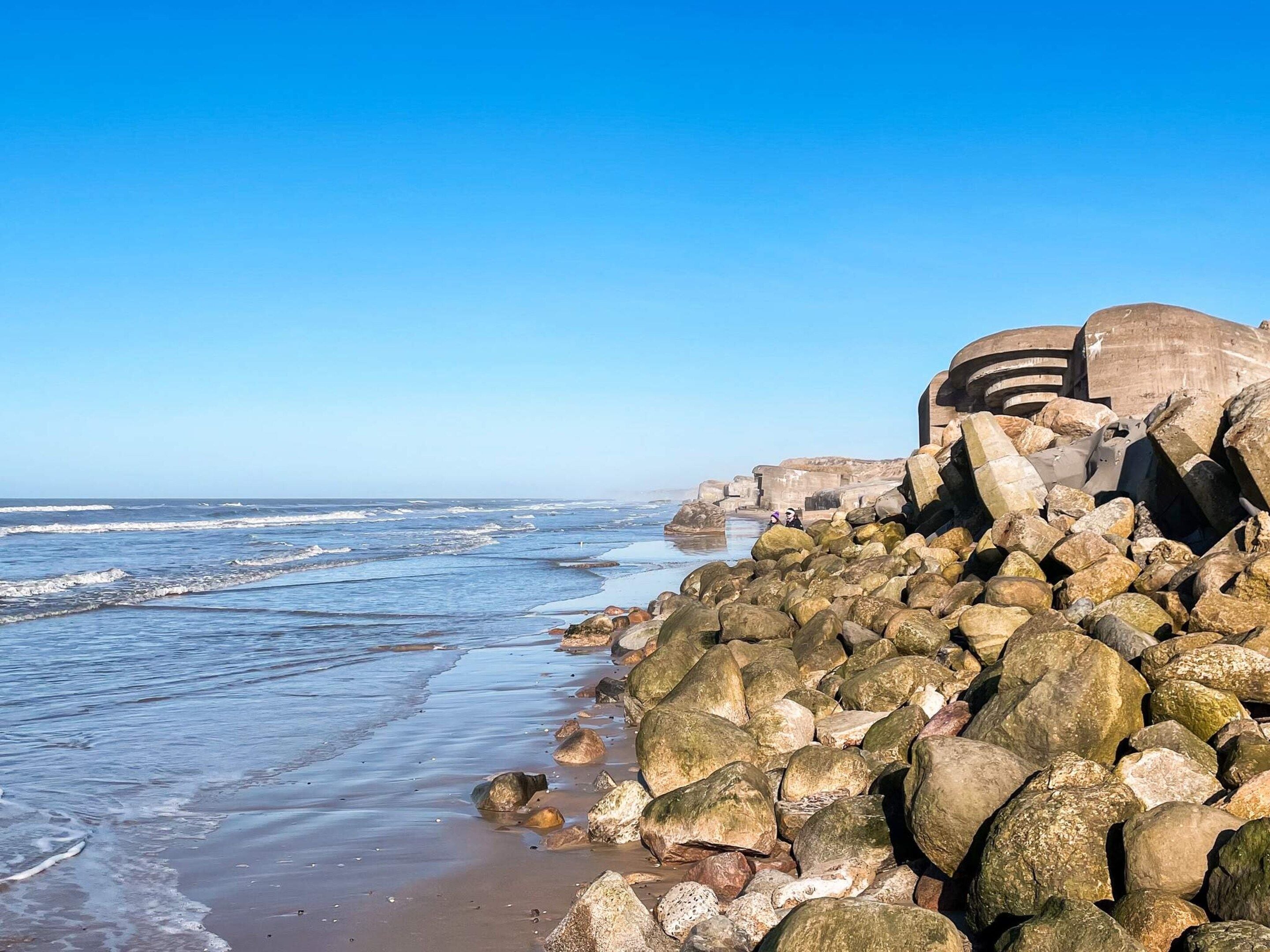 A rocky shoreline with waves, a clear sky, and large boulders.