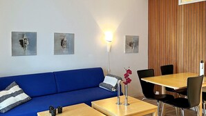A room with a blue sofa, two wooden tables, a dining table with chairs, and wall-mounted artwork. - 4 Star Holiday Home in Lokken (Lokken)