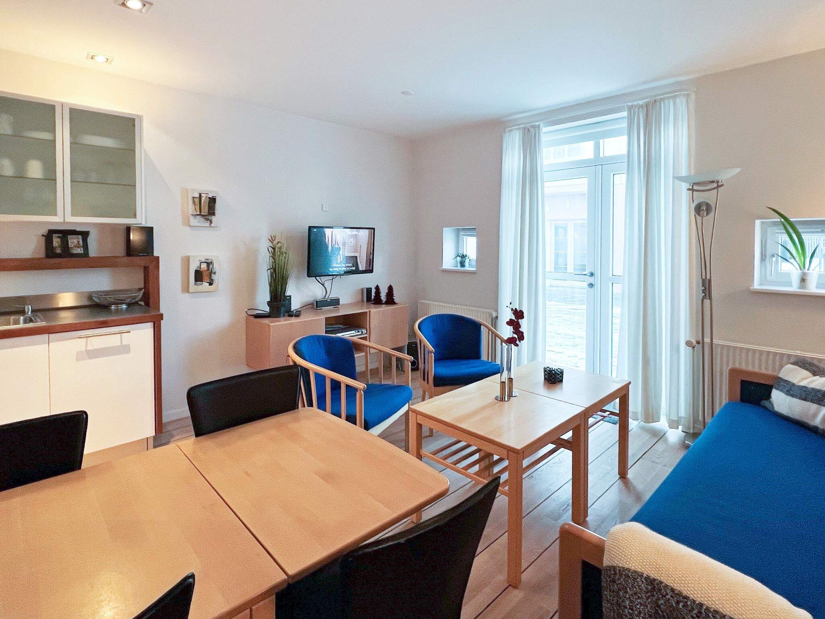 Ein modernes Wohnzimmer mit Esstisch, blauen Stühlen, einer Couch und einem Fernseher.