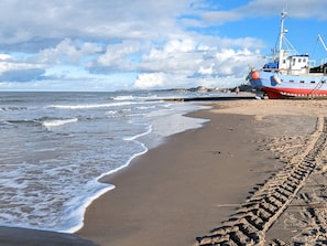 A beach with a shipwreck and footprints leading to it. - 4 Star Holiday Home in Lokken (Lokken)