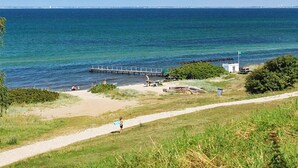 Un sendero costero que lleva a una playa con un muelle que se adentra en el agua, rodeado de vegetación.