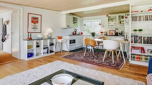 Una cocina moderna con armarios blancos, un comedor con mesa y sillas blancas, una estantería llena de libros y una alfombra blanca en el suelo.