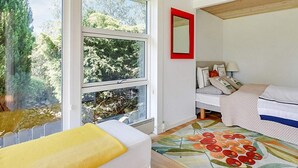 Un dormitorio con cama, mesita de noche, ventana y espejo con marco rojo.